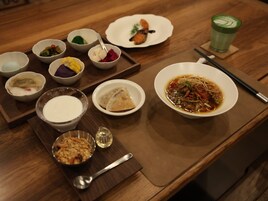 A wooden table with various dishes including a bowl of soup, several small bowls with different foods, and a green drink.