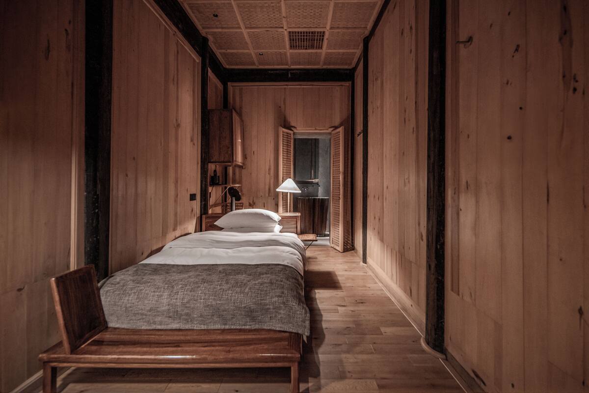 A narrow hallway with wooden walls and a bed at the end.