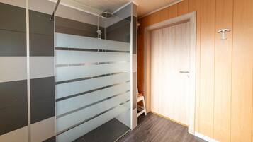 Bathroom features a glass partition with horizontal lines, a showerhead mounted on the ceiling, and a small stool.