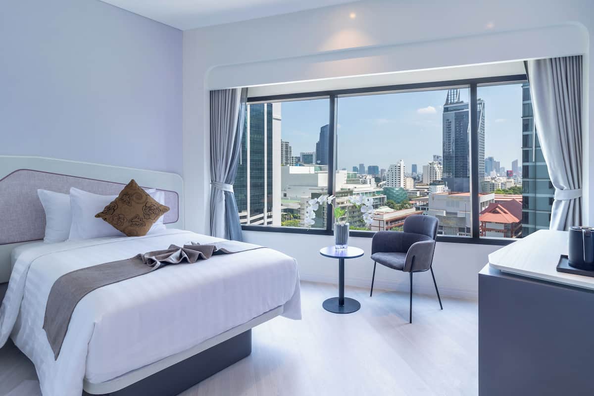 A hotel room with a large window, a bed, a chair, and a small table.