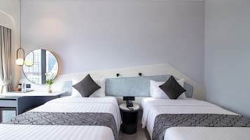 A hotel room with two beds, a desk, a chair, a round mirror, and a small table with a vase of flowers.