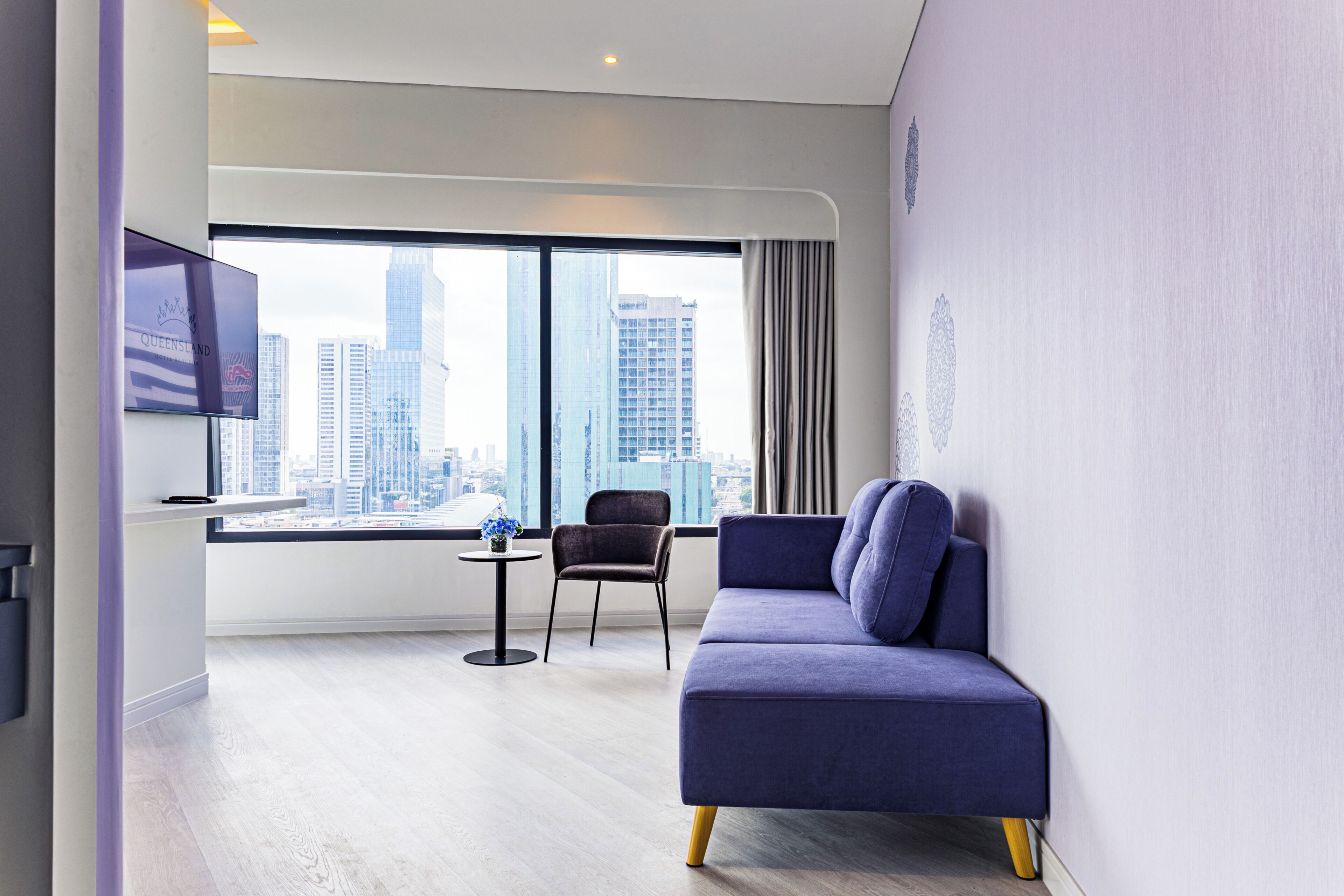 Ein modernes Hotelzimmer mit großem Fenster, einer Couch, einem Sessel und einem kleinen Tisch.