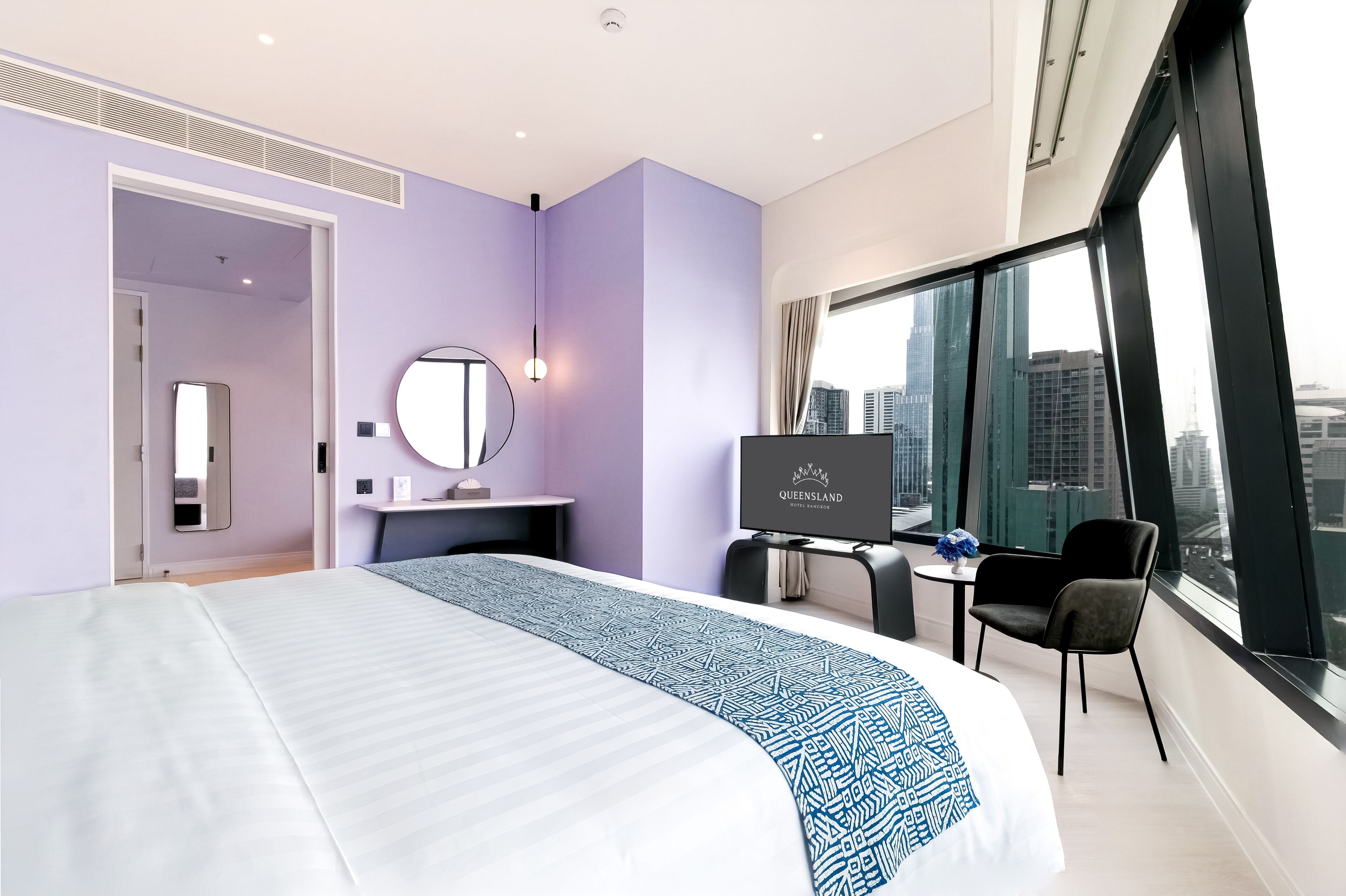 Habitación de hotel moderna con una cama grande, un escritorio, televisión y vistas a la ciudad.