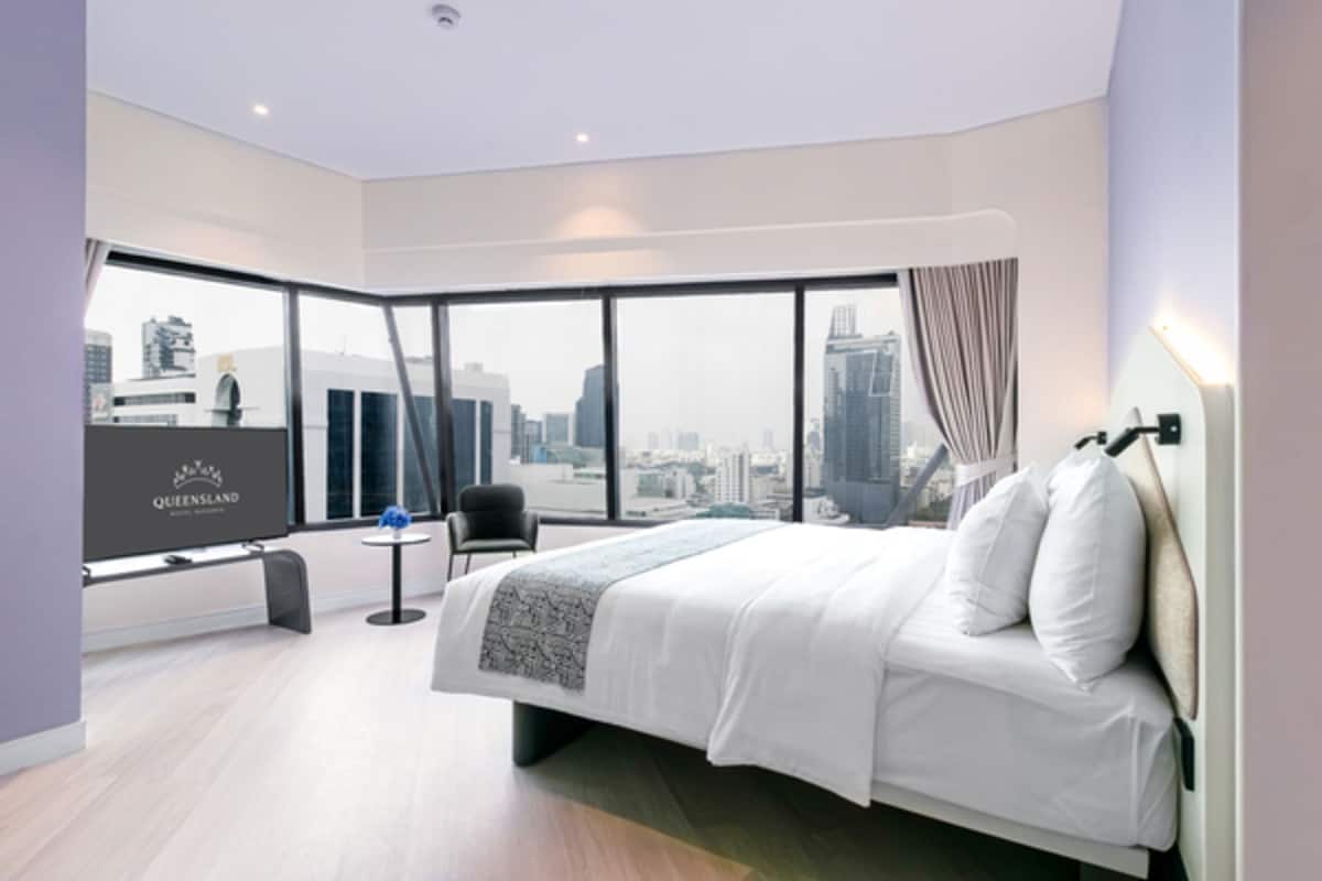 A modern hotel room with a large bed, a city view, a small table, and a chair.