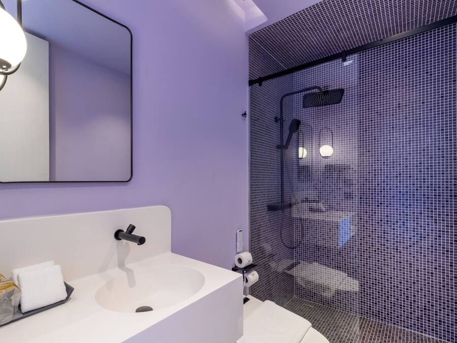 Un baño con lavamanos blanco, espejo y cabina de ducha con puerta de vidrio tipo malla.