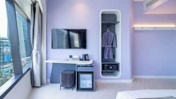 Habitación de hotel moderna con un ventanal grande, televisión de pantalla plana, pequeña cocina, armario con bata y cama.