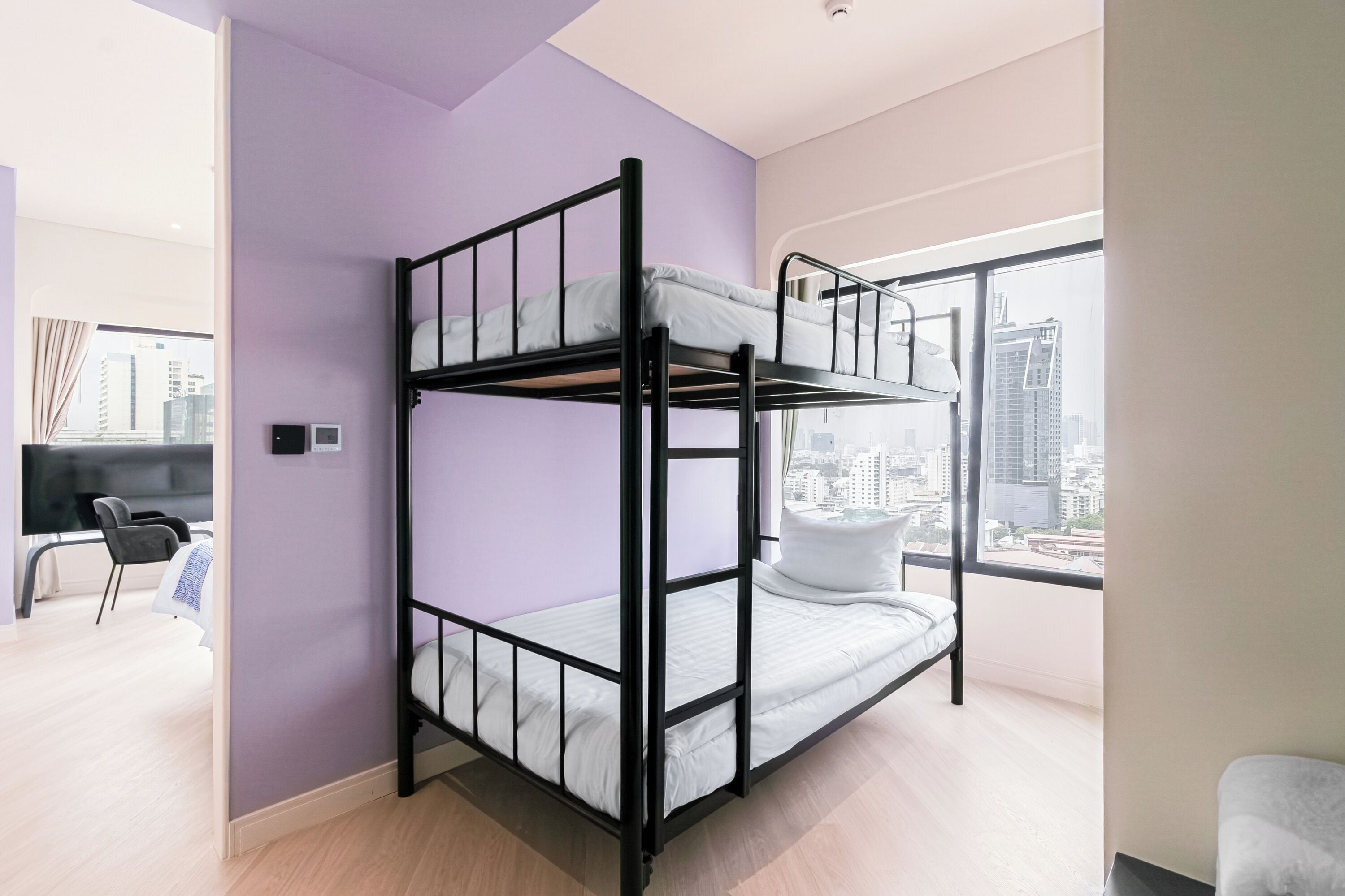 A bunk bed in a room with a city view, a desk, and a chair.