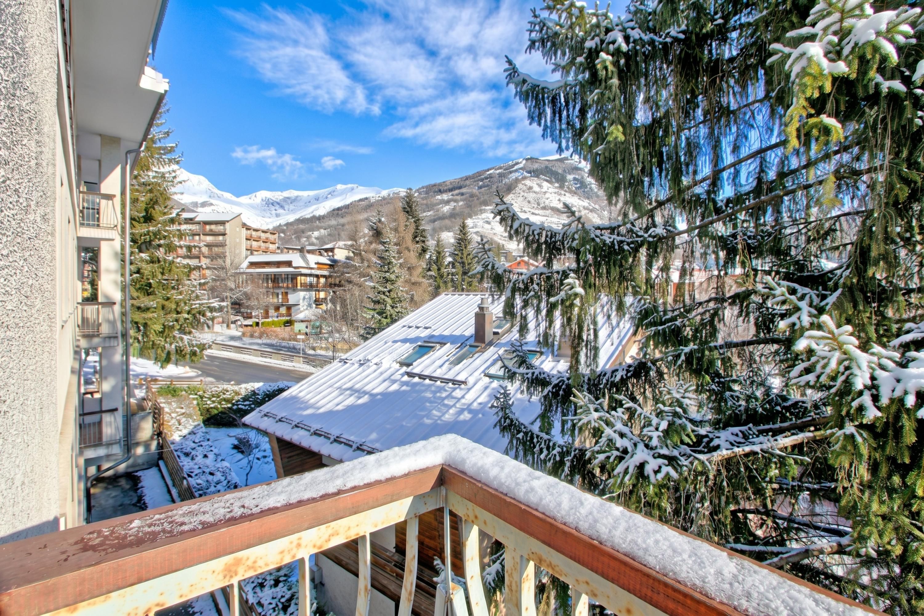 A balcony with a metal railing overlooking a snowy mountain landscape, buildings, and a clear blue sky.