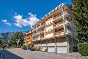A multi-story building with balconies, a parking area, and a mountain backdrop. - La Casa Di Felice (Bardonecchia)