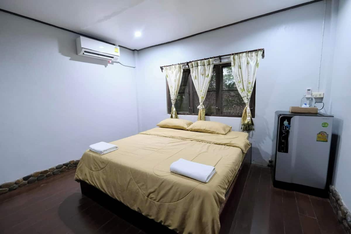 Une chambre à coucher avec un lit, des rideaux, un climatiseur et un réfrigérateur.