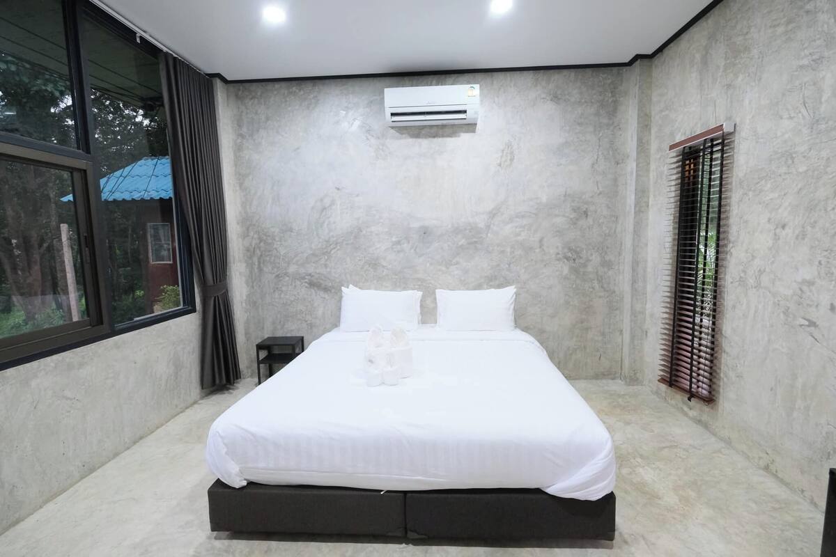 Une chambre moderne avec un grand lit, un appareil de climatisation, une fenêtre avec des stores et une vue sur l’extérieur.