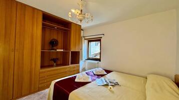 Habitación de hotel con cama, armario de madera, radiador y ventana con vistas.