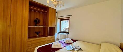 Une chambre d’hôtel avec un lit, une armoire en bois, un radiateur et une fenêtre donnant sur un paysage agréable.