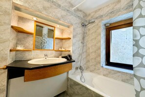 A bathroom with a white sink, a mirror, a shower, and a window.