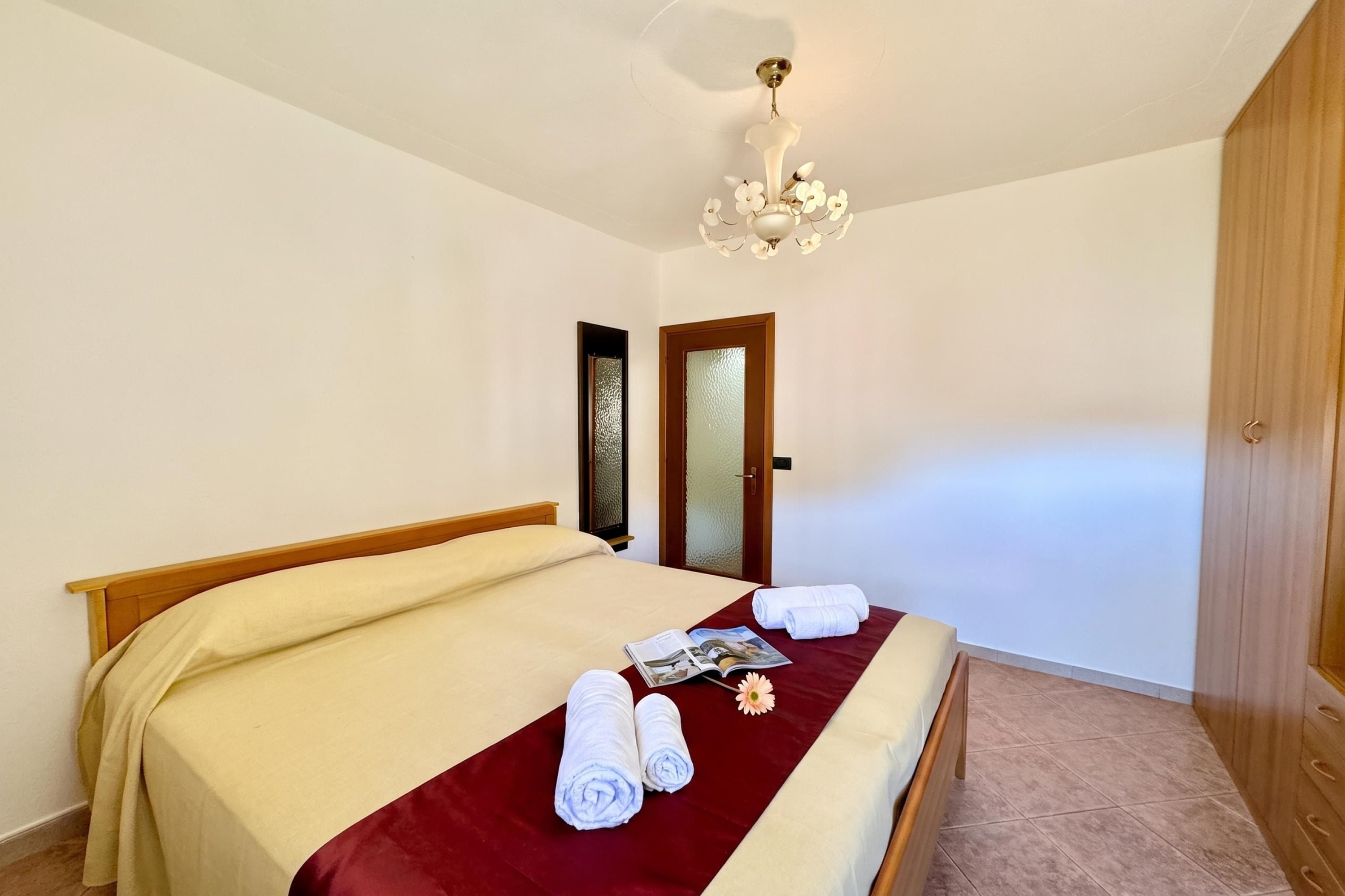Habitación de hotel con cama, un armario de madera, una puerta con panel de vidrio esmerilado y un candelabro.