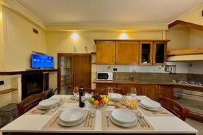 Comedor con una mesa preparada para cuatro personas, un televisor y una cocina al fondo.