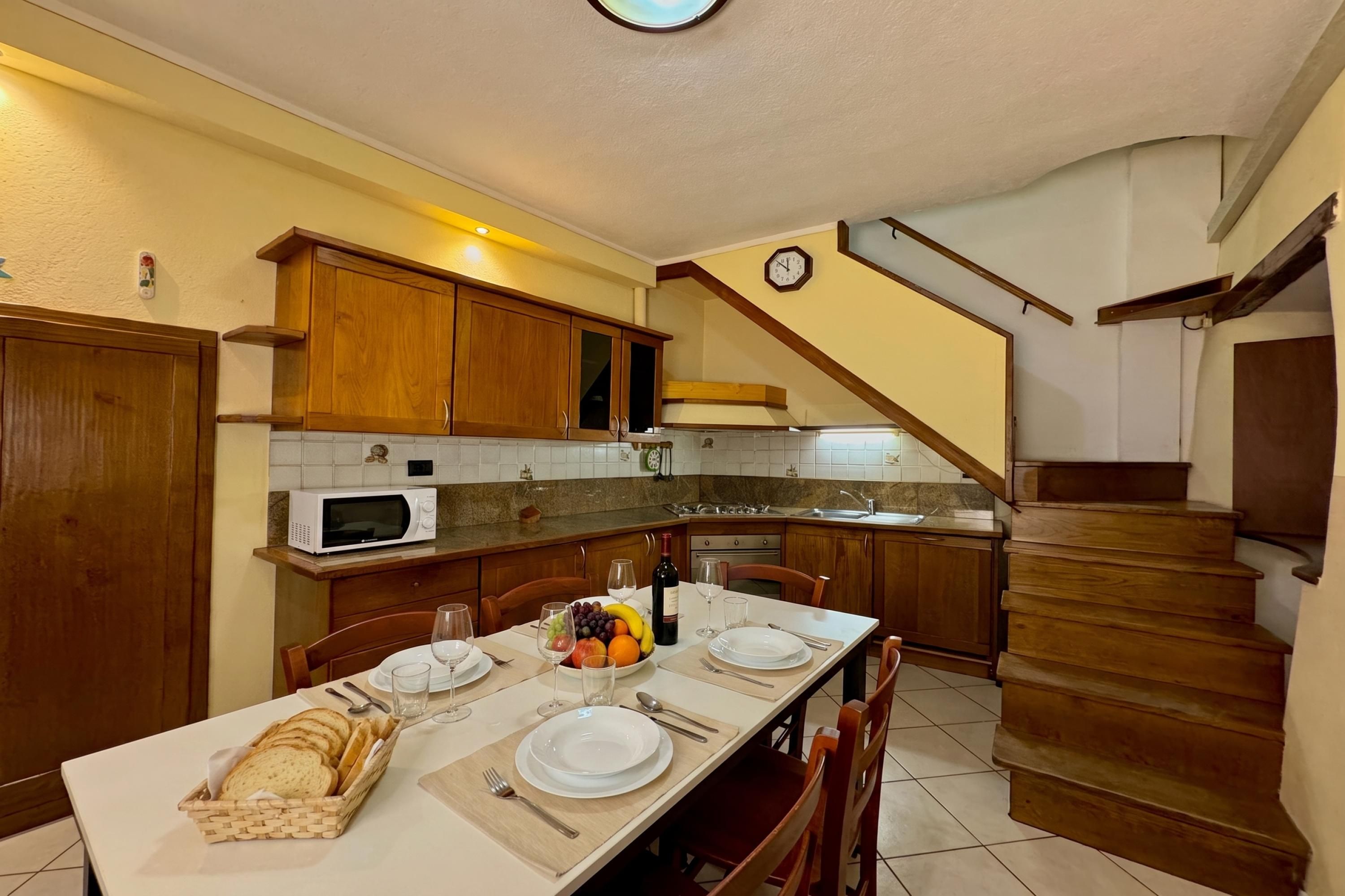 A kitchen with wooden cabinets, a microwave, a dining table set for four, and a staircase leading to another level.