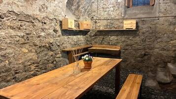 Un interior rústico de piedra con mesas y bancos de madera, una ventana pequeña y estanterías de madera con letreros.