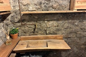 A rustic stone wall with a wooden bench and a small table with a plant and reed diffuser. - Borgo di Porlezza (Porlezza)