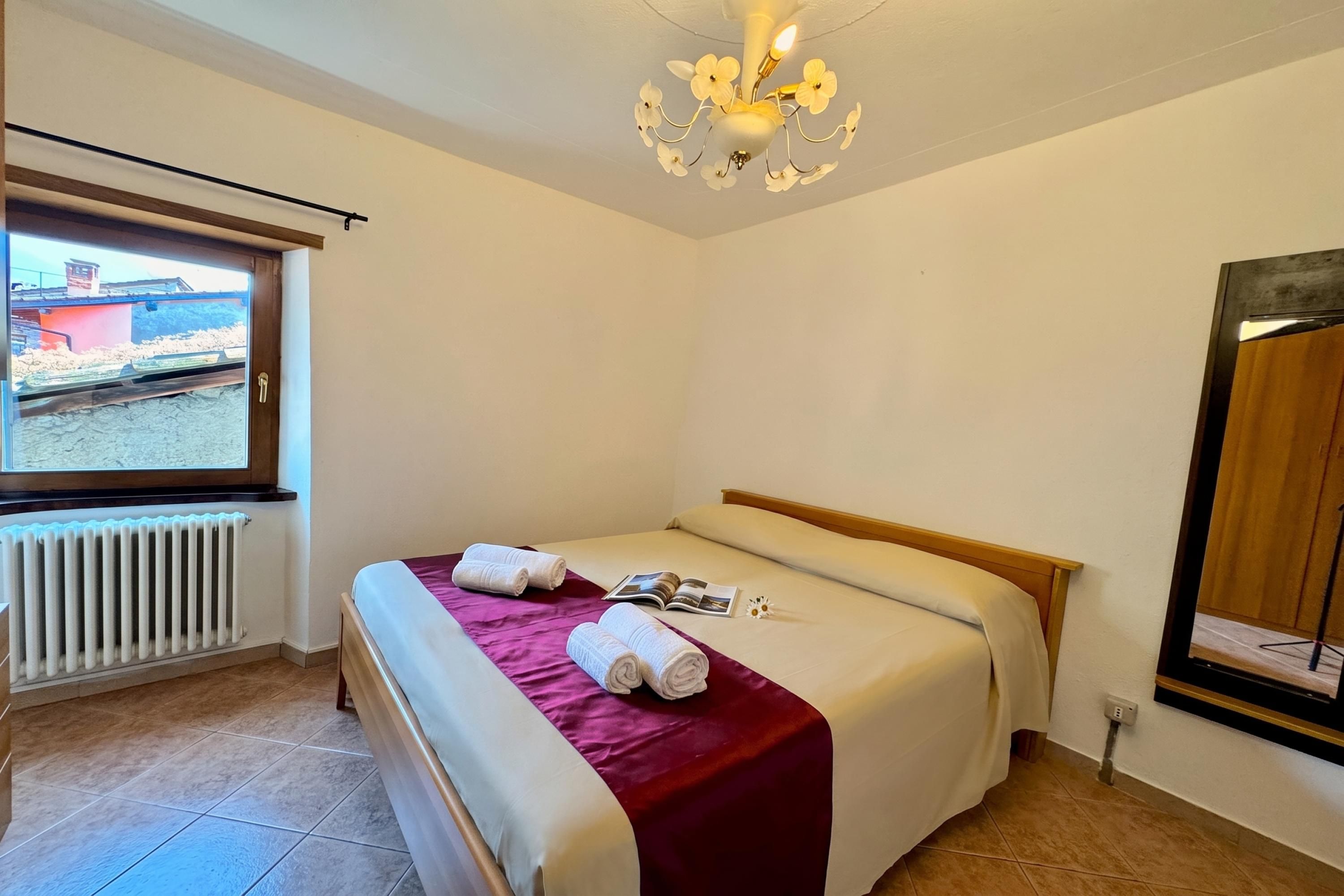 Habitación de hotel con cama, ventana, radiador y candelabro.