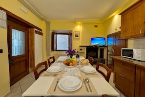 A dining area with a table set for four, a television, and a microwave in the kitchen area.