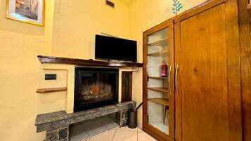 Una sala de estar con chimenea, un televisor montado encima y un mueble de madera con puertas de vidrio.