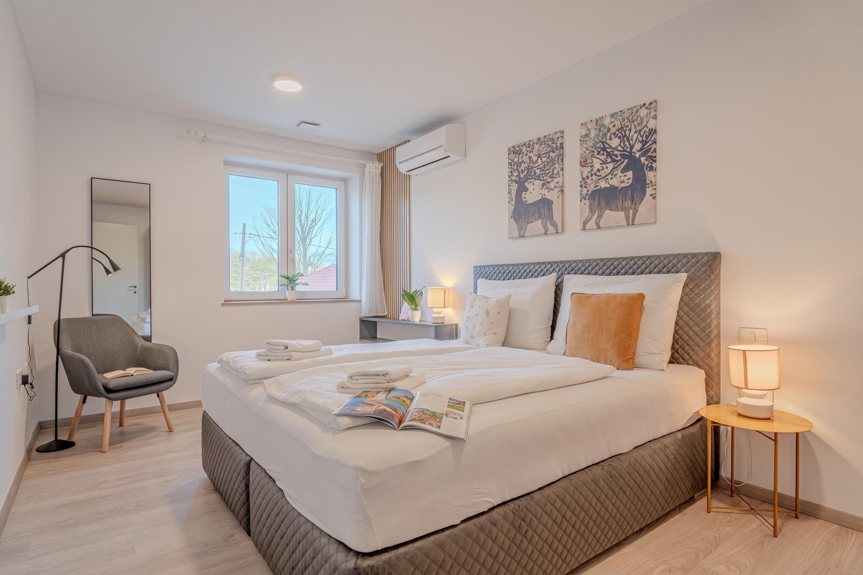 A modern bedroom with a large bed, bedside tables, a chair, and artwork on the walls.