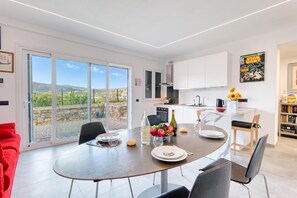 Een moderne keuken met witte kastjes, een eethoek met een ronde tafel, en een grote schuifdeur die uitkomt op een prachtig uitzicht.
