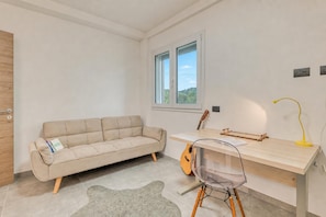 Una habitación moderna con un sofá, un escritorio, una guitarra y una silla transparente.