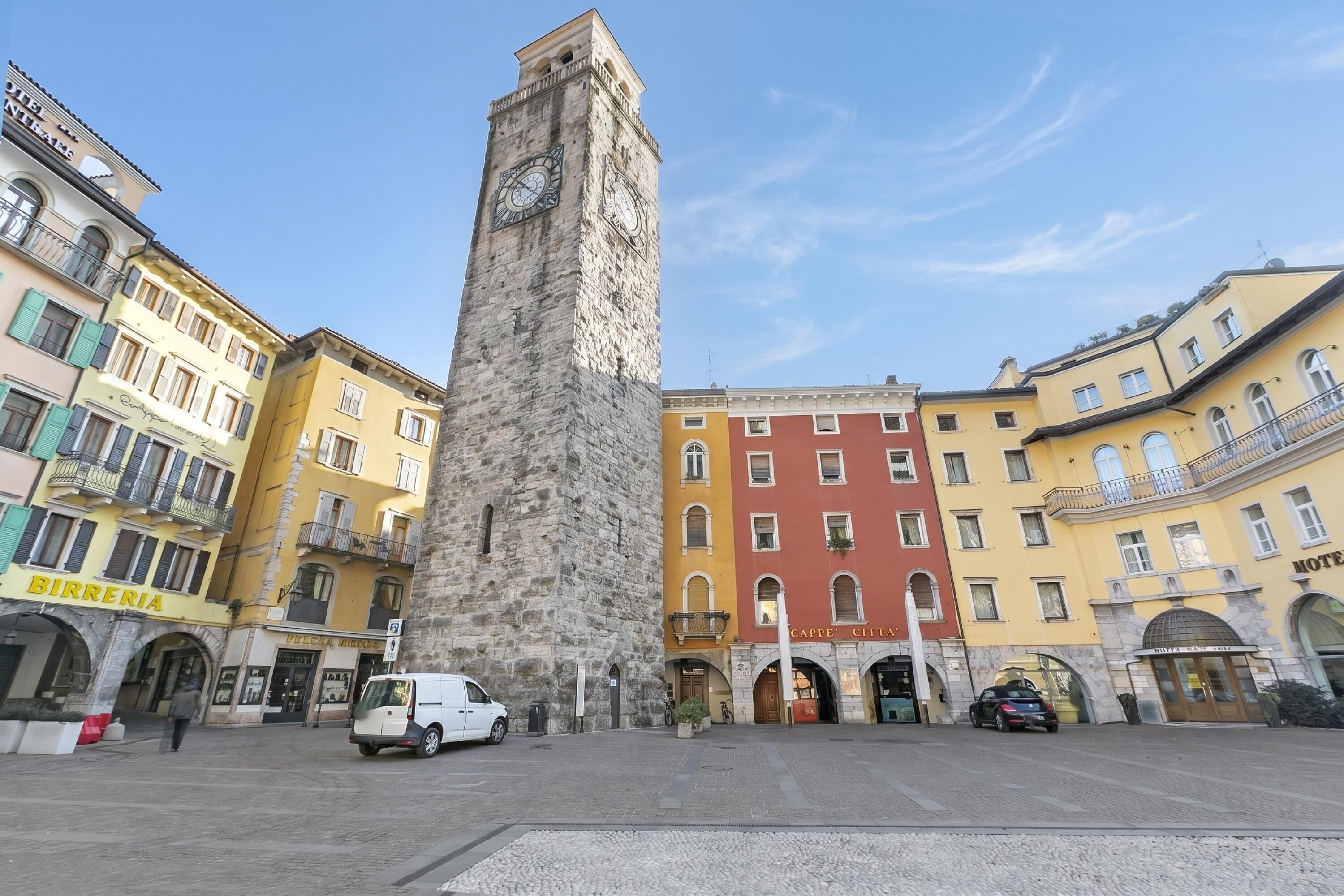 A historic tower with a clock, surrounded by colorful buildings with various storefronts.