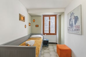 A bedroom with a bed, a small table, a radiator, a window, and a poster on the wall.