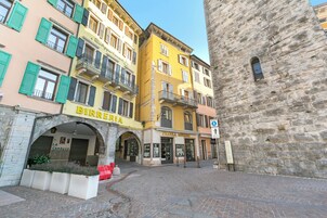 A cobblestone street with historic buildings, including a bakery named "BIRREARIA" and a pharmacy "PICCOLA MURANO".