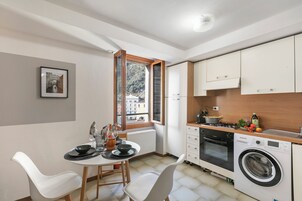 A compact kitchen with a dining area, a washing machine, and a window with a view of buildings.