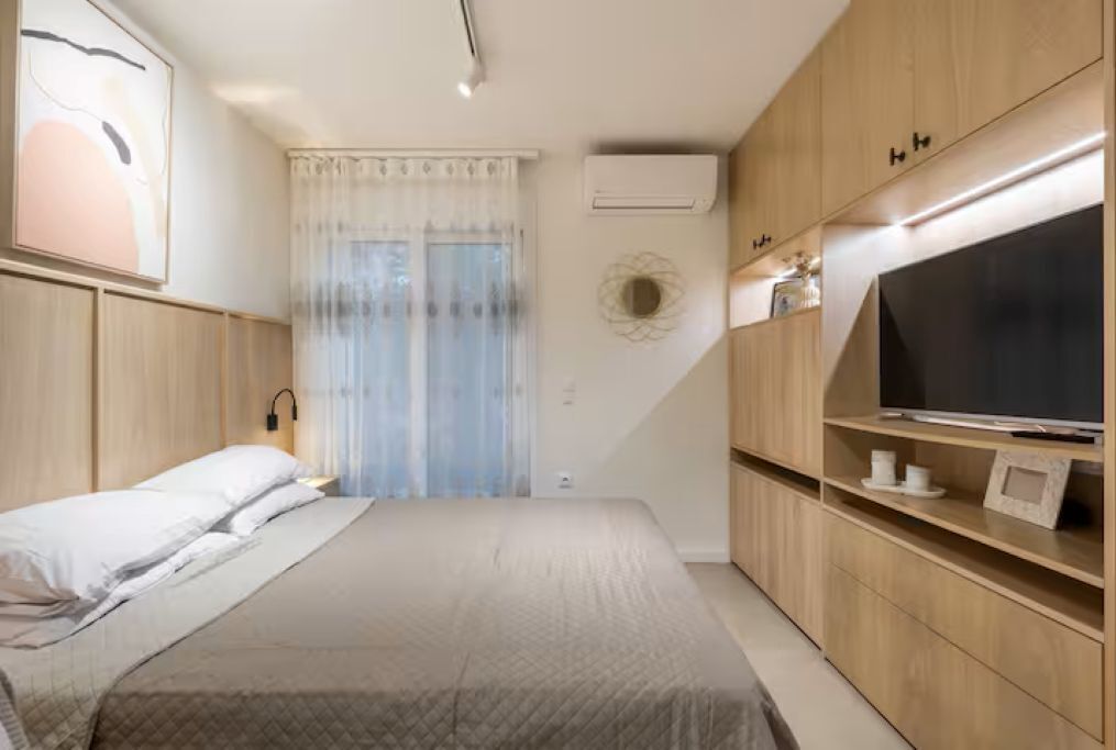 A bedroom with a bed, a TV, wooden cabinets, and a window with curtains.