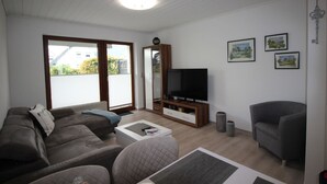 A modern living room with a sofa, a TV, and a grey armchair. - Ferienhaus in Busum fur 4 Personen (Büsum)