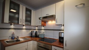 A modern kitchen with white cabinets, a stainless steel sink, a built-in oven, and a coffee maker. - Ferienhaus in Busum fur 4 Personen (Büsum)