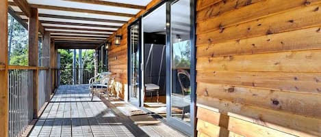 Fachada de madera con porche cubierto, puertas corredizas de vidrio y mobiliario exterior.