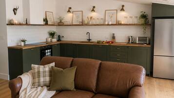 A modern kitchen with dark green cabinets, a brown leather sofa, and a wooden countertop.