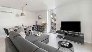 A modern living room with a grey sofa, dining area, and a TV on a black stand. - Corte di Ascona Apartments (Ascona)