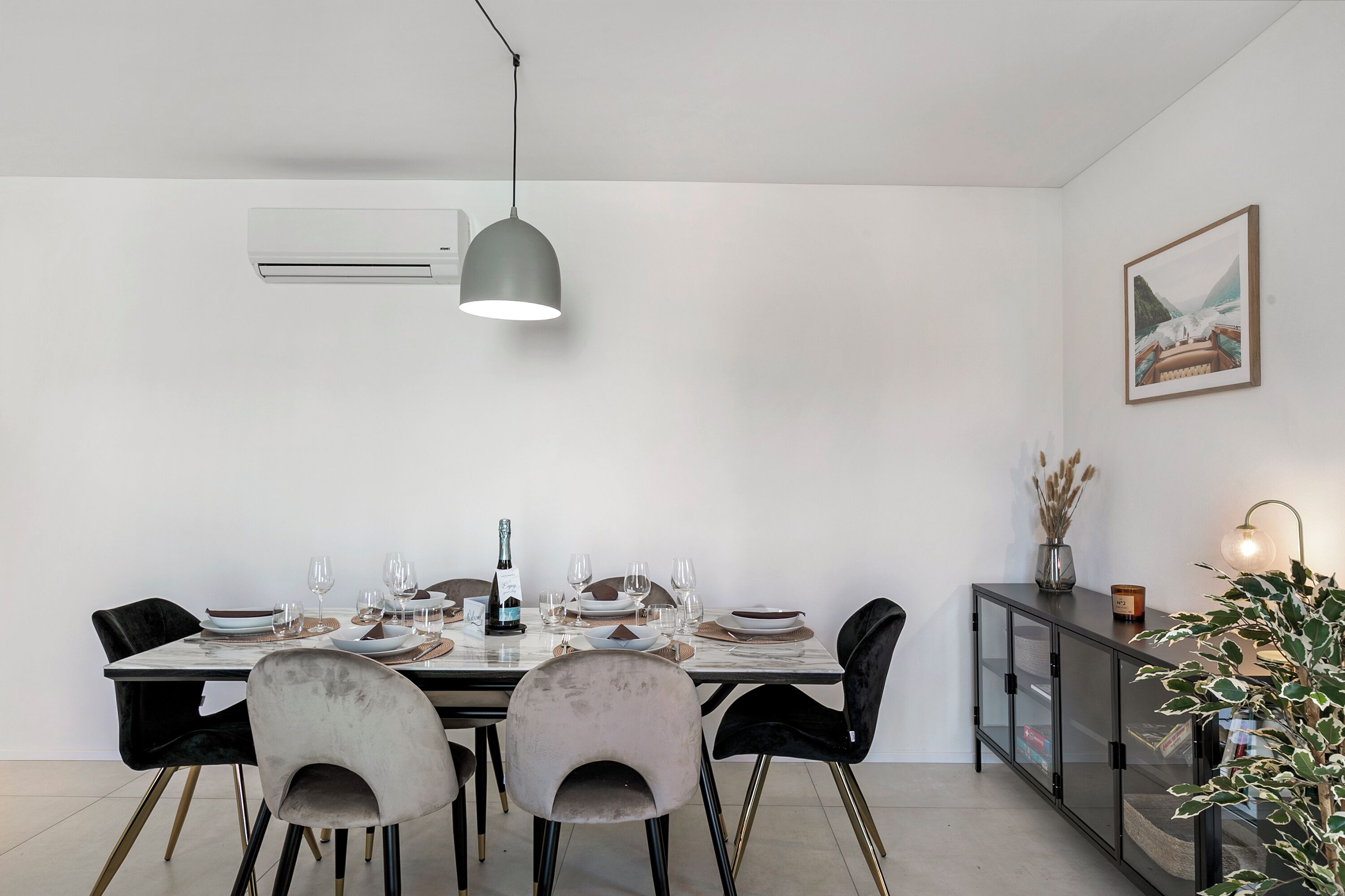 A dining area with a table set for six, a modern pendant light, and a cabinet with a vase and candle.