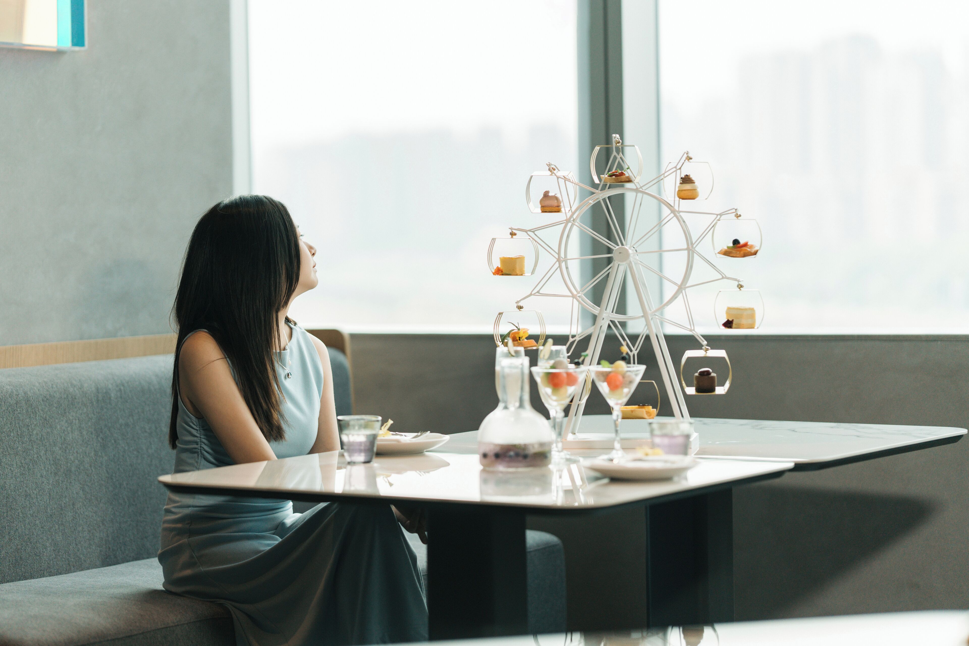 Una mujer sentada a una mesa con una fuente de postres, un vaso de agua y un plato de comida.