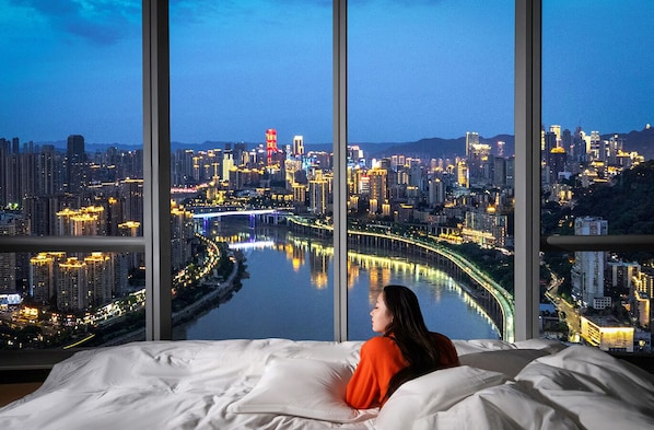 Una cama con un ventanal grande con vista a un paisaje urbano nocturno.