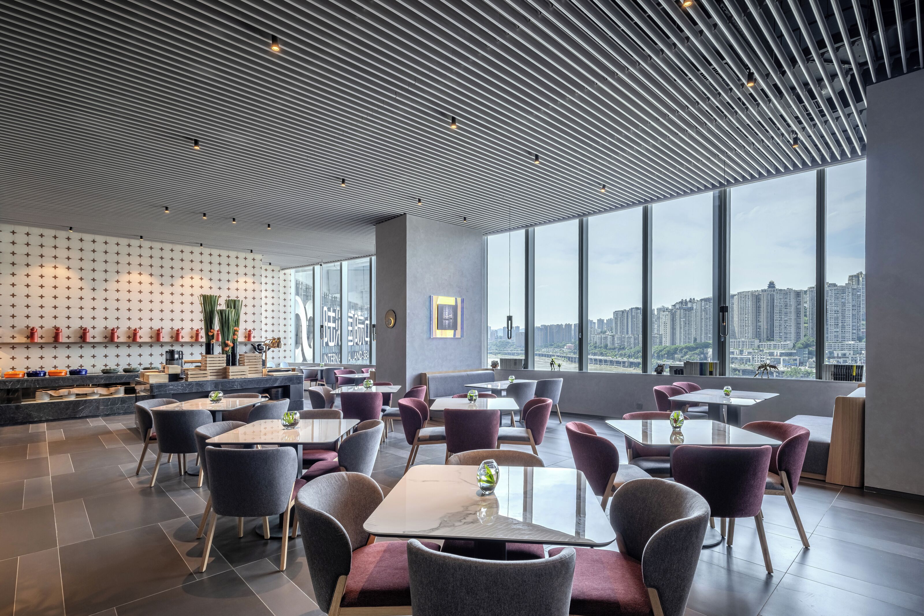 Un restaurant moderne offrant une vue sur la ville, avec un mur décoré de motifs, des tables et des chaises.