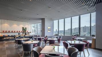 Un restaurant moderne offrant une vue sur la ville, avec un mur décoré de motifs, des tables et des chaises.