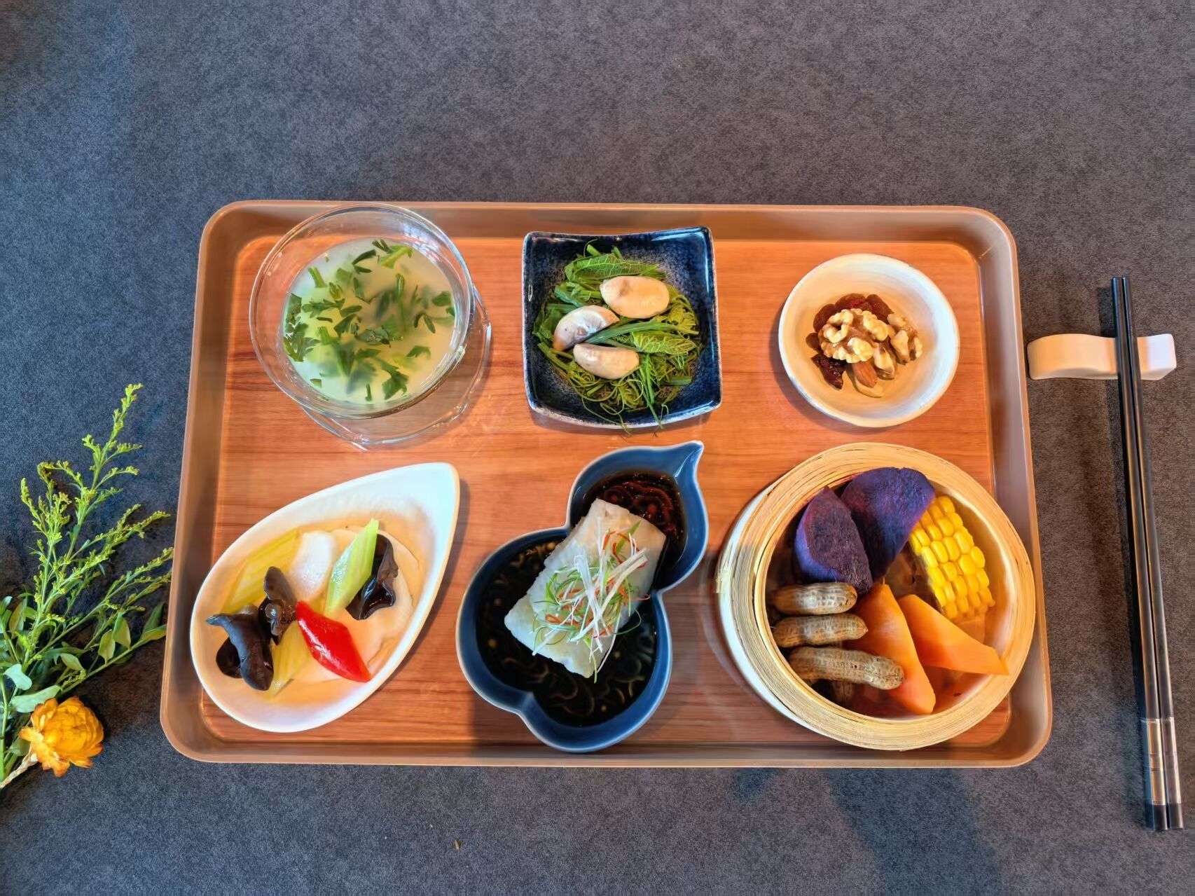 A tray with various food items including a bowl of soup, a plate with vegetables, a dish with peanuts, and a bowl with corn and other vegetables.