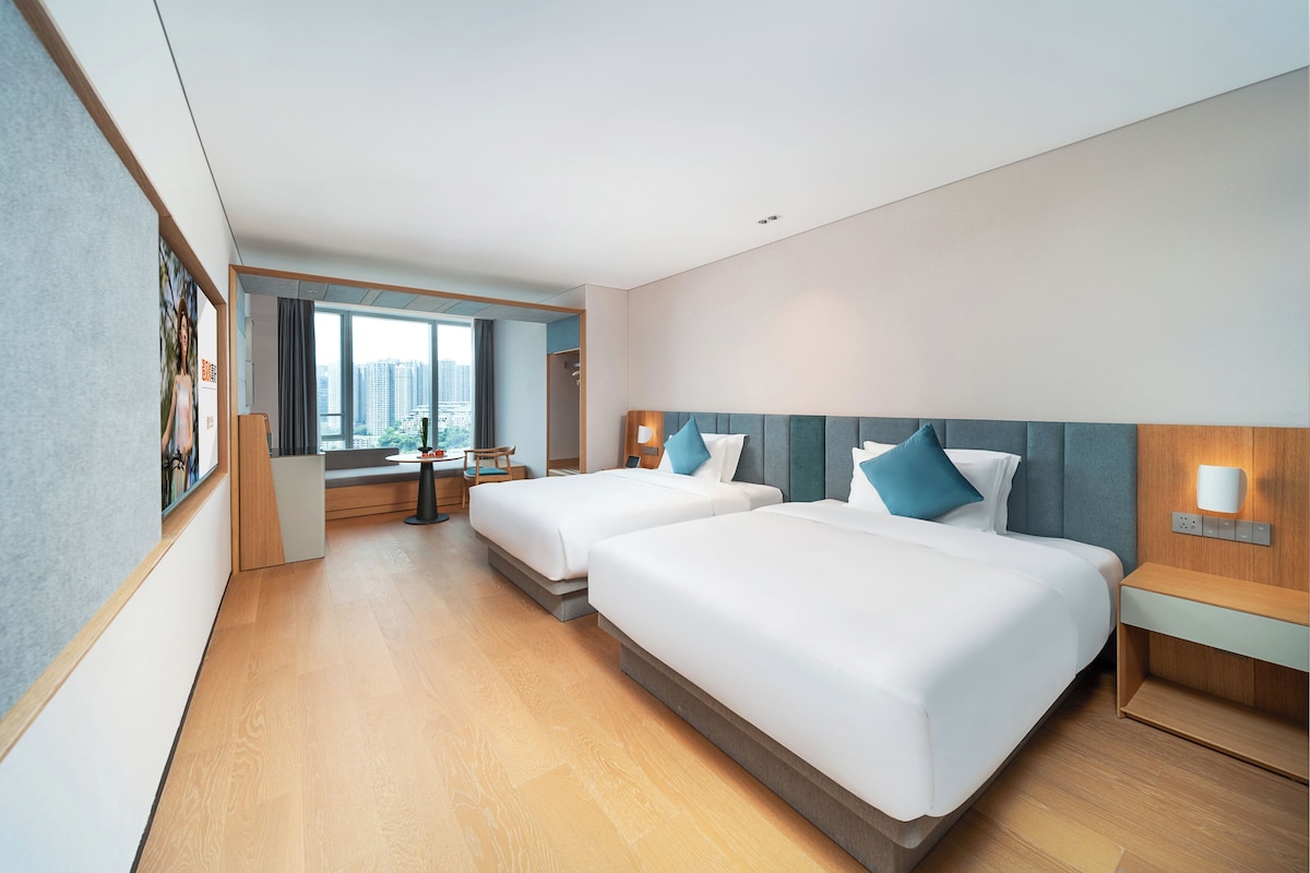 Una habitación de hotel moderna con dos camas, un escritorio y vistas a la ciudad.
