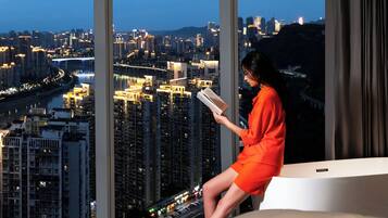 Une personne assise près d’une fenêtre, avec vue sur la ville, est en train de lire un livre.