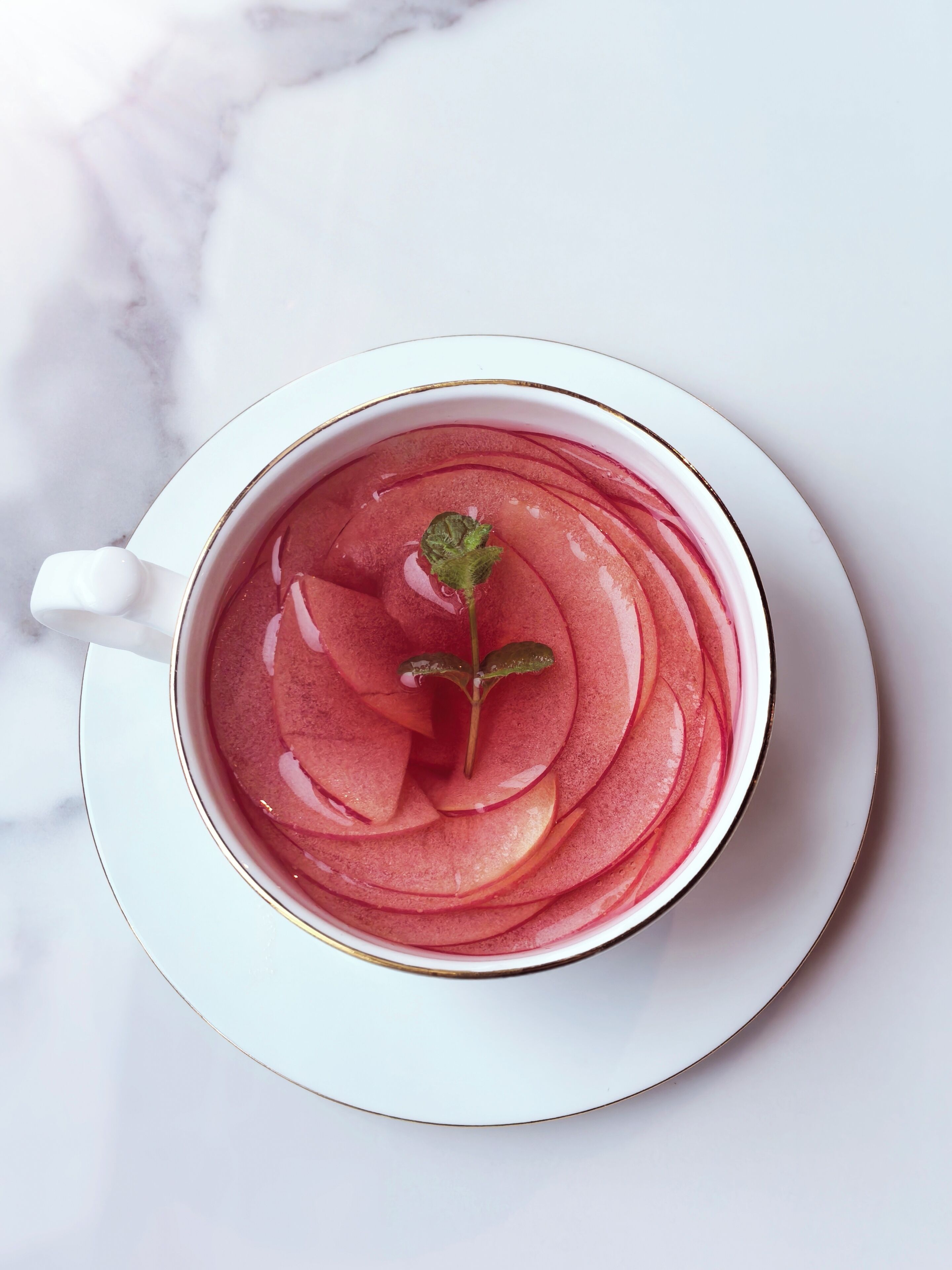 A cup of pink beverage with a leaf garnish on a white saucer.