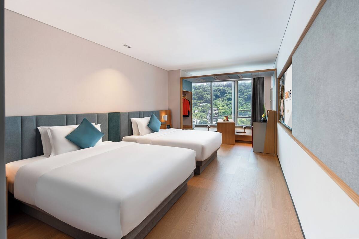 Habitación de hotel con dos camas, un escritorio y vista a zonas verdes.