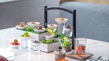 Una mesa de comedor con diversos alimentos y bebidas, incluyendo tazones de frutas, una taza de té y una bandeja con cubiertos.